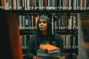 A woman in a cap and gown holding a stack of books